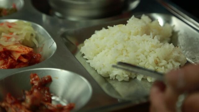 한국의 구내식당 식판 위에 담긴 흰 쌀밥과 김치, 반찬을 젓가락으로 집으려는 모습 근접 촬영 핸드헬드 브이로그 영상