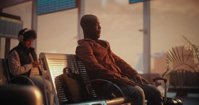 Relaxed African American Traveler Stretching And Looking at Airplanes Through Airport Window. Man Raises Arms to Stretch Muscles, Easing Tension of Travel, Gazes Out of Window At Airplanes on Runway.