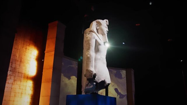 Side profile of a monumental statue of Ramses II displayed in a dark museum, dramatically lit with lens flare and immersive historical backdrop.