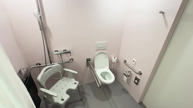 Wide view of accessible hospital bathroom with toilet, shower chair, and support rails. Concept for accessibility, patient care, and safety.