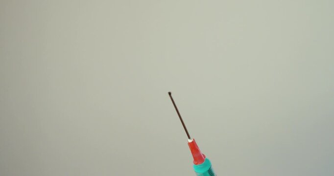 Close-up of syringe spraying liquid from needle tip. Concept for medical use, drug misuse, addiction, and pain treatment.
