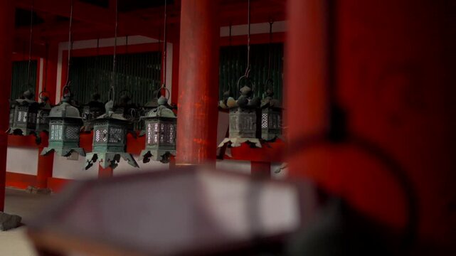 Panning shot starting from green metal lanterns in the temple corridors of Kasuga Taisha Shrine in Nara, Japan, moving through the gardens to reveal the temple facade on a cloudy winter day.