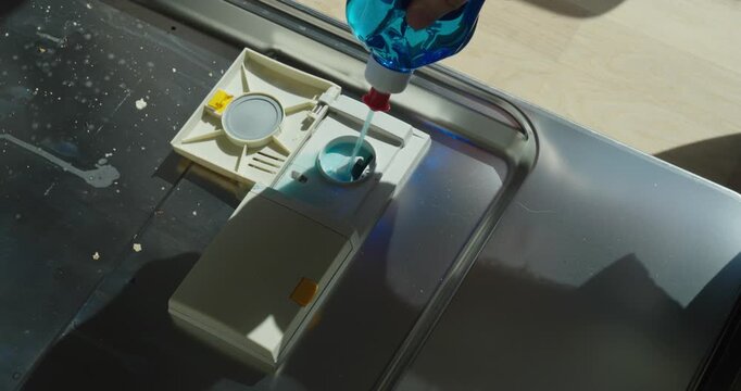 Close-up of pouring rinse aid into dishwasher compartment. Concept for cleaning, maintenance, and household care.