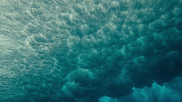 Underwater of breaking ocean wave creating dense bubbles and foam, side angle medium slow motion, pulsating cloud formation