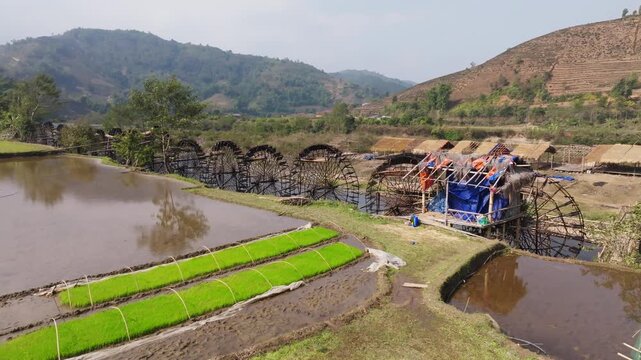 Traditional bamboo water wheels at Guồng Nước N&agrave; Khương - Bản Bo rotate beside the river, lifting water toward nearby rice paddies in a rural mountain valley in northern Vietnam.
