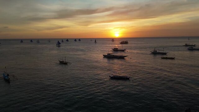 Aerial view of the iconic Paraw sailboats at sunset off the coast of Boracay Island, Philippines. Dozens of traditional boats gather on the calm ocean during a golden tropical evening.