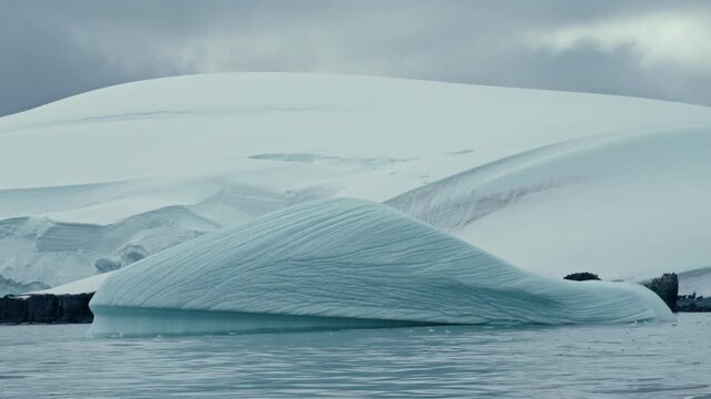 Beautifully sculpted low iceberg with intricate wave-like erosion patterns floating in turquoise Antarctic waters with snowy dome mountain behind