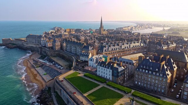 Saint Malo Intra Muros in Ille et Vilaine Brittany France with dense granite buildings and slate roofs leading toward Saint Vincent Cathedral spire above ramparts and Le Manche, drone forward glide