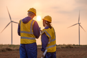 Engineer team using laptop at wind turbine farm during sunset, analyzing renewable. © eakgrungenerd