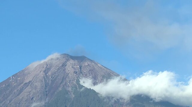 A dramatic drone timelapse captures white clouds sweeping across the active volcanic summit of Mount Merapi in Central Java