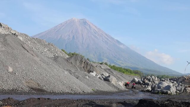 An adventurous group of tourists drives ATVs across a rocky riverbed at the base of the majestic Mount Semeru in East Java