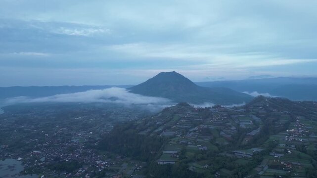 A cinematic drone shot pans slowly to the right, revealing the breathtaking vastness of the Lake Batur caldera and the iconic Mount Batur volcano in Bali