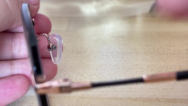 Hands awkwardly using a miniature screwdriver to rotate an already loosened small screw covered in green oxidation during a home eyeglasses repair.