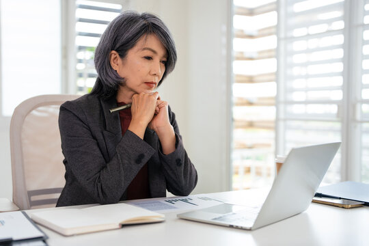 Focused concentrated middle aged businesswoman thinking over problem, staring at laptop screen, reading email, making difficult decision, watching video, webinar, studying online