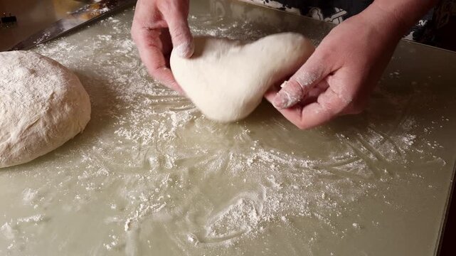 Close-up of hands working with a ball of dough on a floured surface, preparing for baking
