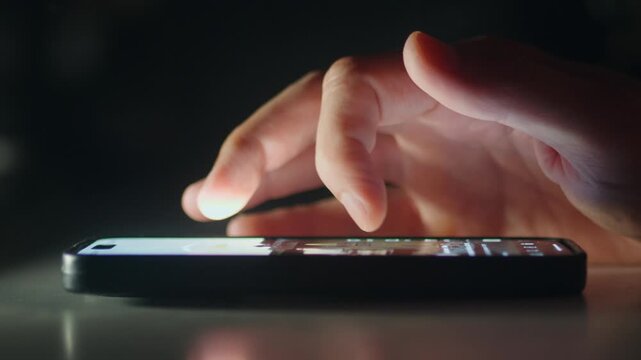 Close up finger tapping smartphone touchscreen in dark light shows mobile technology and digital interaction night. Phone screen glow highlights online browsing social media scrolling mobile app use.