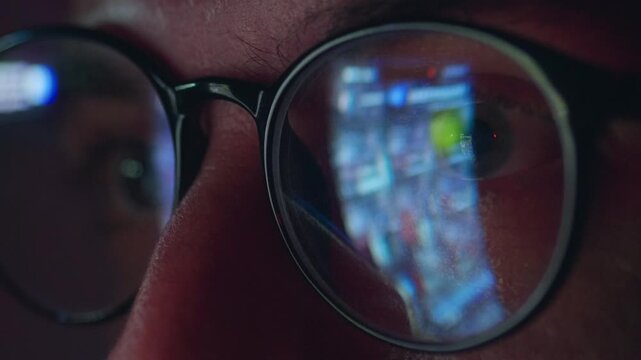 Close up male eyes in glasses reflecting smartphone screen with fast scrolling news feed. Concept of digital information consumption constant media monitoring and endless search for online news update