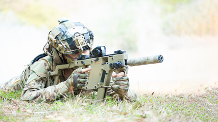 Obraz premium Camouflaged Soldier Resting with Rifle and Helmet in Grassy Field ? Focused Military Preparedness and Operational Readiness Concept, Utilizing Advanced Gear and Tactical Positioning.
