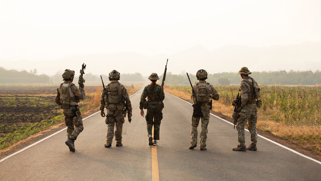 Five U.S. Soldiers in Camouflage Carrying Rifles and Equipment Walk Through a Hazy Field During Military Training, Demonstrating Operational Readiness and Focused Teamwork in a Secure Environment