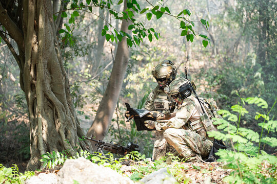 Two Soldiers Reviewing Tactical Map with Machine Gun in Dense Forest Terrain During Operational Assessment, Preparing for Combat Deployment. Two soldiers, wearing camouflage fatigues, are intently exa