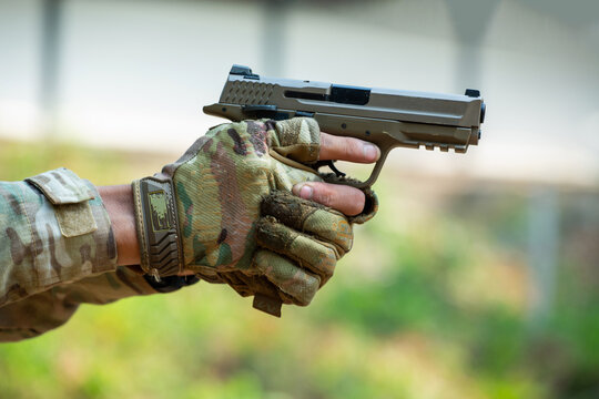 Two Individuals Discuss Tactical Strategy with Smith & Wesson Handgun in Dark Environment, Wearing Camouflage Gloves and Tactical Wristband, Suggesting Preparedness and Vigilance.