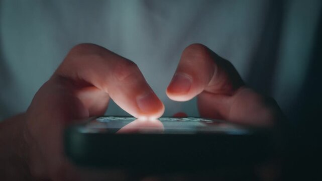 Male hands messaging on smartphone in low light scene with glowing screen and dark background. Messaging on mobile phone represents instant communication private chat and everyday digital interaction