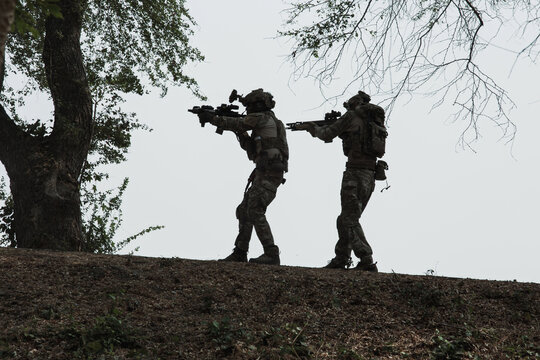 Two Soldiers Conducting Combat Training with Tactical Gear on a Green Hill, Engaging in Live-Fire Exercises with Camouflage Weapons and Utilizing Protective Eyewear in a Simulated Training Environment