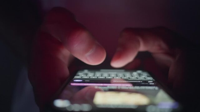 Male hands typing message on smartphone keyboard in close up while holding mobile phone in dark environment. Smartphone messaging shows digital communication modern lifestyle, social media interaction