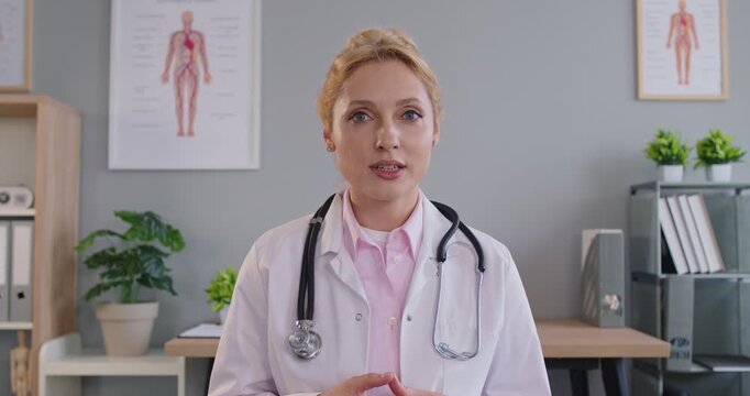 Female doctor looking at camera having online video call or conference with colleague or sick patient sitting in medical office. Telemedicine and consultation online concept. 4k video.