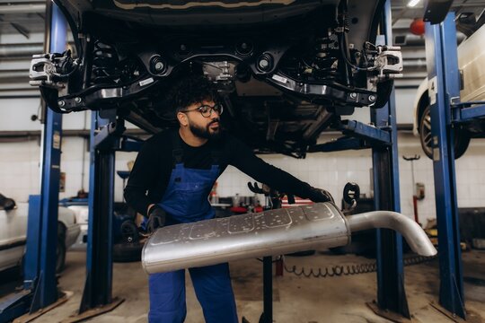 Auto mechanic replacing car exhaust muffler in garage