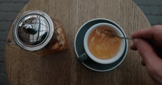 POV, top view of a male hand stirring a hot herbal tea with apple slices in a cafe