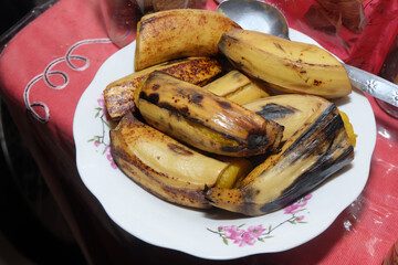 a plate of cooked bananas, likely steamed or lightly grilled, served on a white floral-patterned plate © awgraphoto