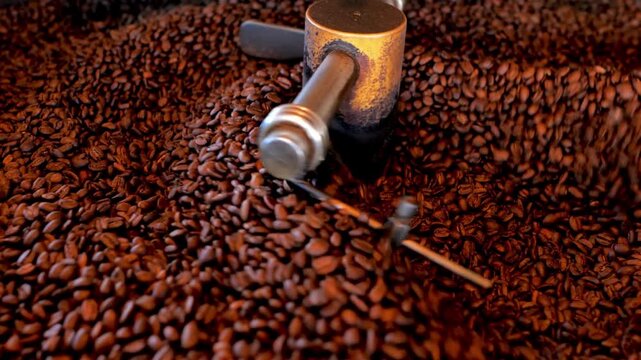 Roasted coffee beans in coffee roaster process Mixing and roasting process - coffee roaster machine during work close-up