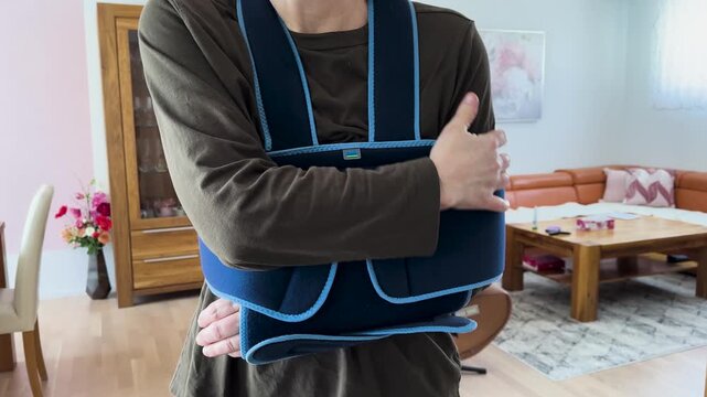Person wearing an arm sling and holding arm at home. Concept for pain, recovery, and rehabilitation.