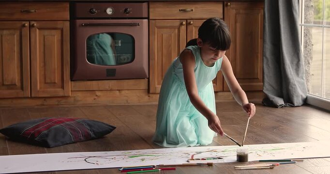 Girl having fun indoors, painting abstract artwork pictures on paper during leisure in domestic kitchen. Self expression through creative artistic activity at home, child development, learning concept