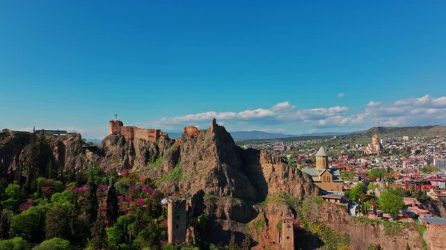 Drone view over Narikala Fortress, Tbilisi, highlighting the ancient defensive walls, elevated position, and dramatic setting above the capital.