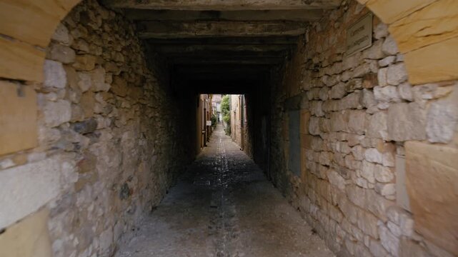Narrow stone passage through a vaulted alleyway in the historic village of Monpazier, Dordogne. The camera moves through the masonry tunnel. Slow motion travelling shot.