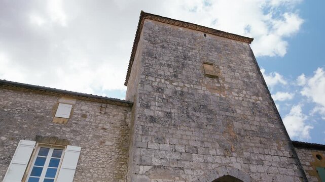 Old stone masonry of a historic building tower reaching towards the sky in Monpazier, Dordogne. Low angle slow motion traveling shot.