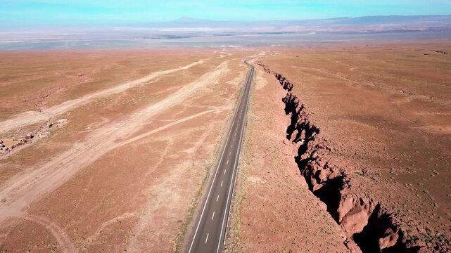 Forward drone flight following a desert highway revealing a vast arid plain with volcanic cones and sparse terrain stretching endlessly to the horizon