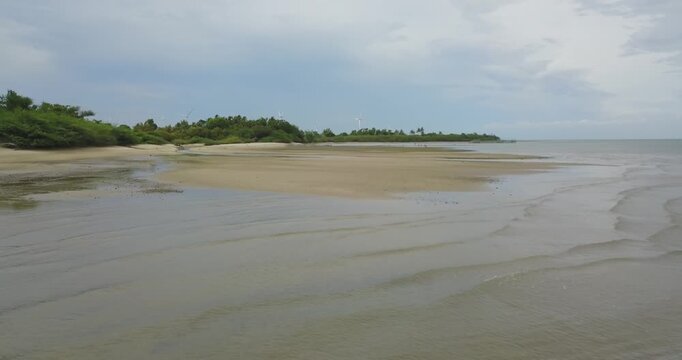 Drone flying very low over shallow water, rocks and sandy shoreline with distant wind turbines barely visible on the horizon in Guimaras Philippines