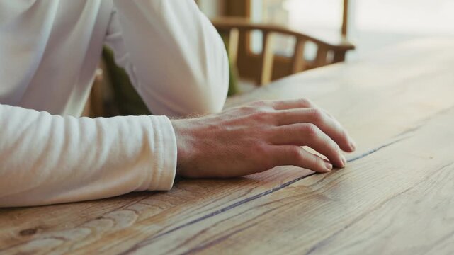 Static tripod shot of a man nervously tapping his fingers on a wooden table