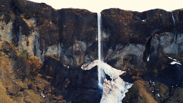 Aerial view of foss a sidu cascade in iceland running off of hills forming scandinavian landscape, nordic scenery. Beautiful icelandic waterfall flowing down snowy mountains. Slow motion.