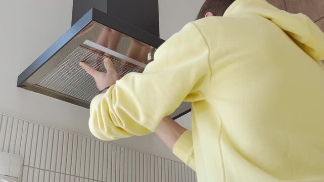 Back view of person replacing metal grease filter in kitchen hood. Concept of appliance cleaning and household maintenance