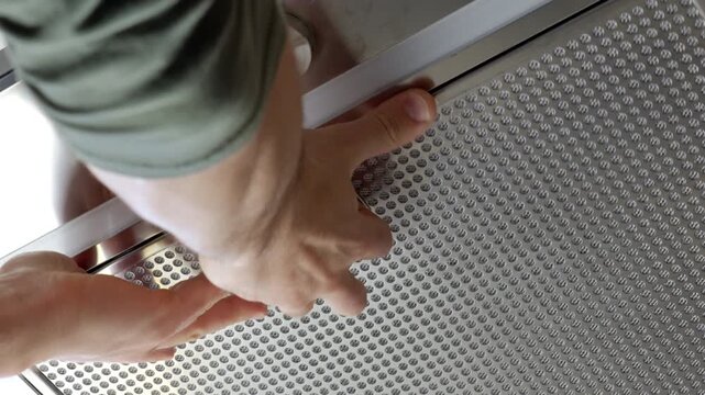 Closeup of hands installing metal grease filter in kitchen range hood. Concept of home maintenance, appliance cleaning and ventilation repair.