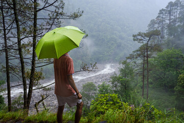 A man stands under a green umbrella in a lush forest near Madhyamaheshwar temple, Uttarakhand, india © 3 Travelers