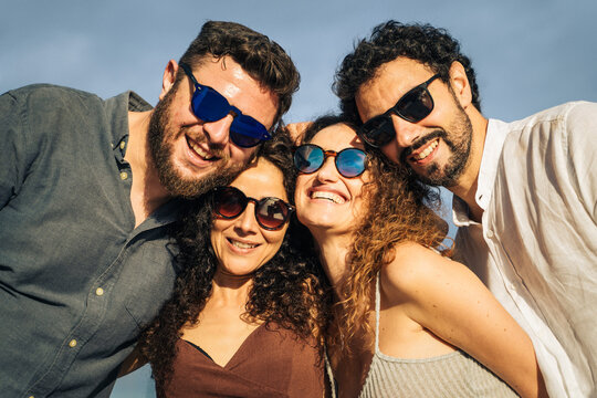 Happy group of adult friends smiling together outdoors in summer. Natural light, casual lifestyle moment showing friendship, trust and genuine connection in a relaxed marina setting.