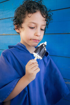 Young boy savoring a delicious ice cream treat against a vibrant blue wall
