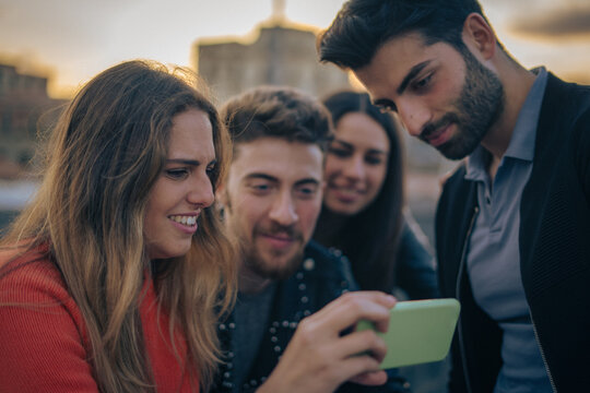 Group of Friends Watching Smartphone Content Outdoors During Sunset