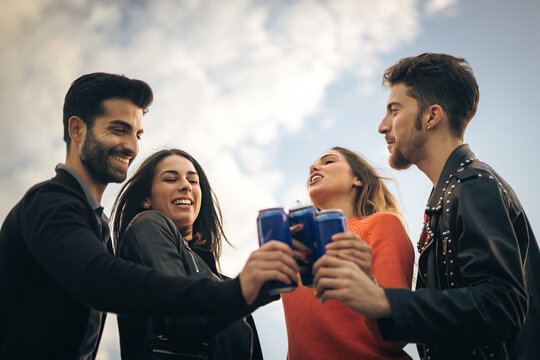 Young friends celebrating together with canned drinks under a beautiful sky.