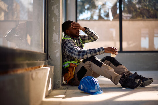 Distraught black worker holding his head in pain at construction site.
